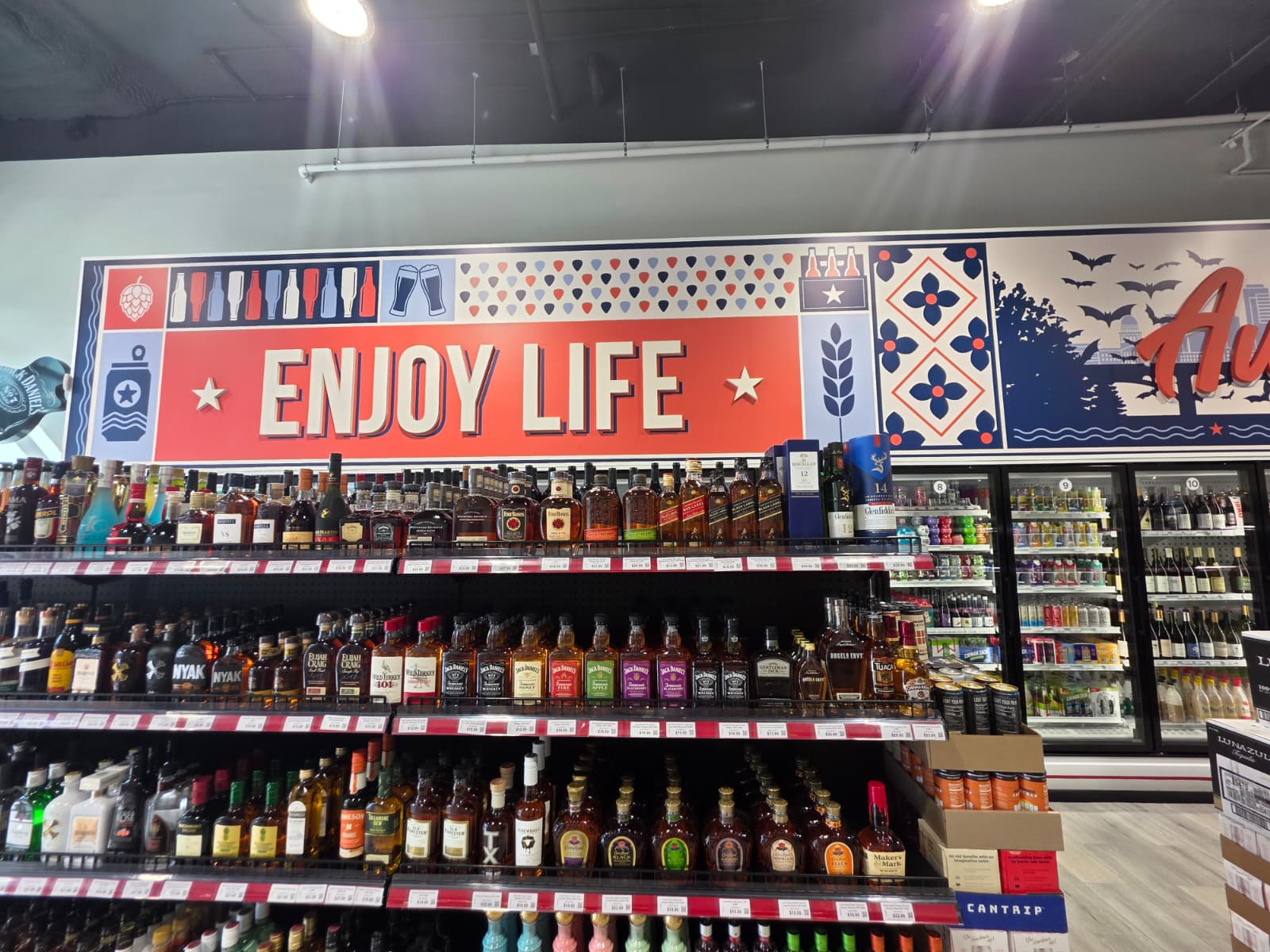 Whiskey and bourbon shelves beneath the Enjoy Life mural