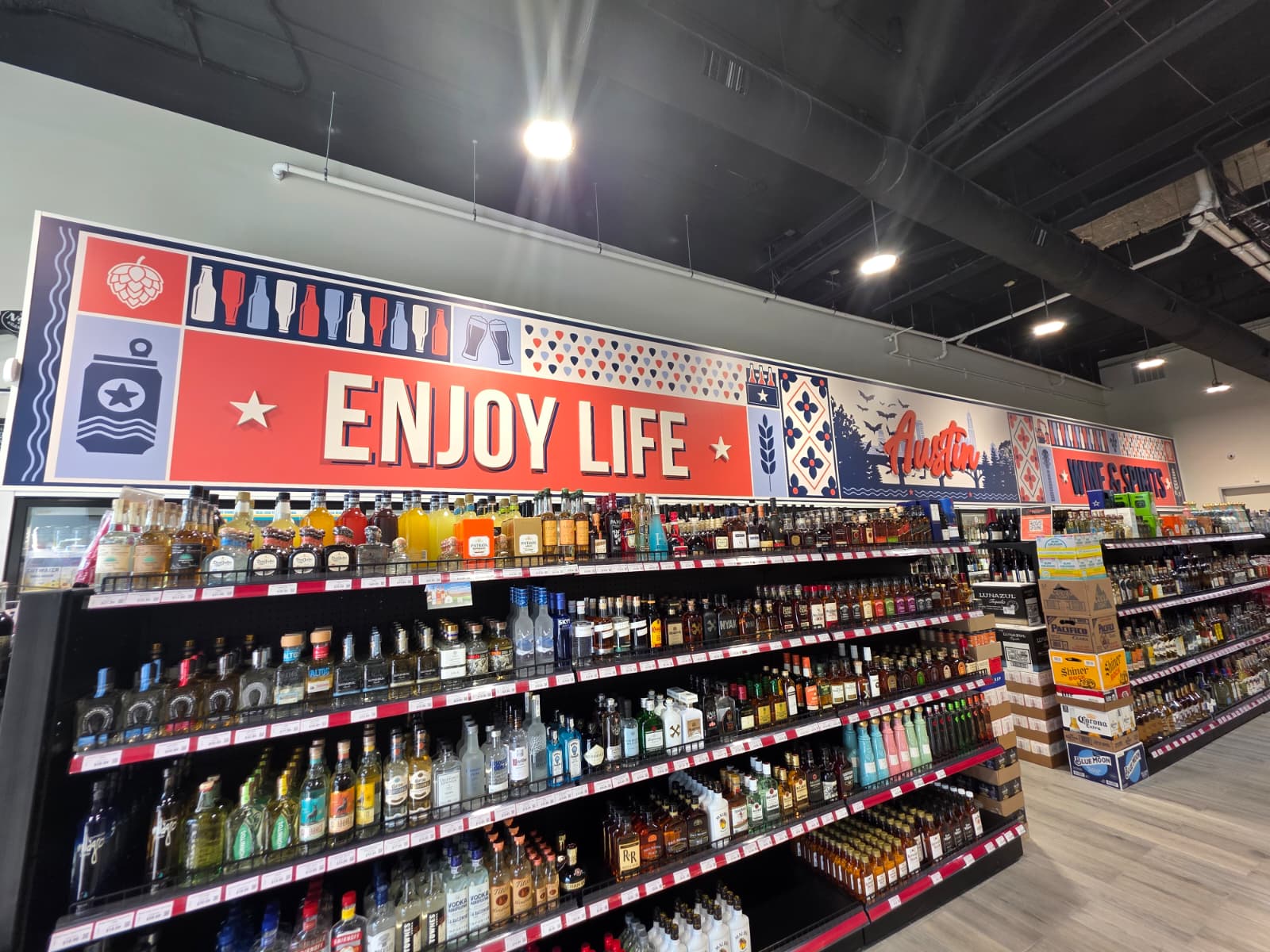 The ENJOY LIFE and Austin murals running above the spirits shelves at East Village Liquor